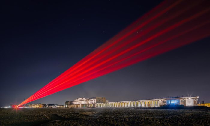 Na belgické pláži svítí bariéra z laserových paprsků poukazující na rozdělení společnosti